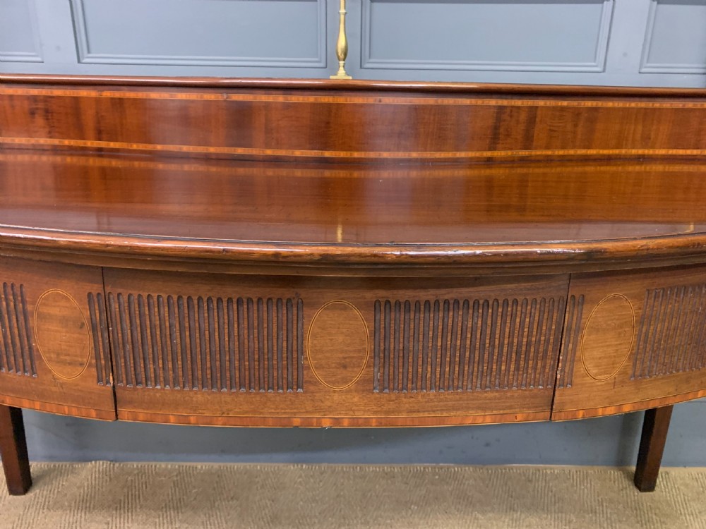 A George III mahogany serving table featuring a serpentine front, inlaid fluted detailing, square tapered legs, and a brass gallery rail. View VIII