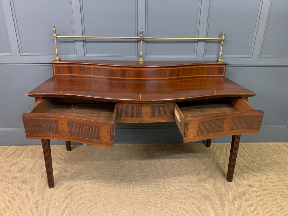 A George III mahogany serving table featuring a serpentine front, inlaid fluted detailing, square tapered legs, and a brass gallery rail. View XII