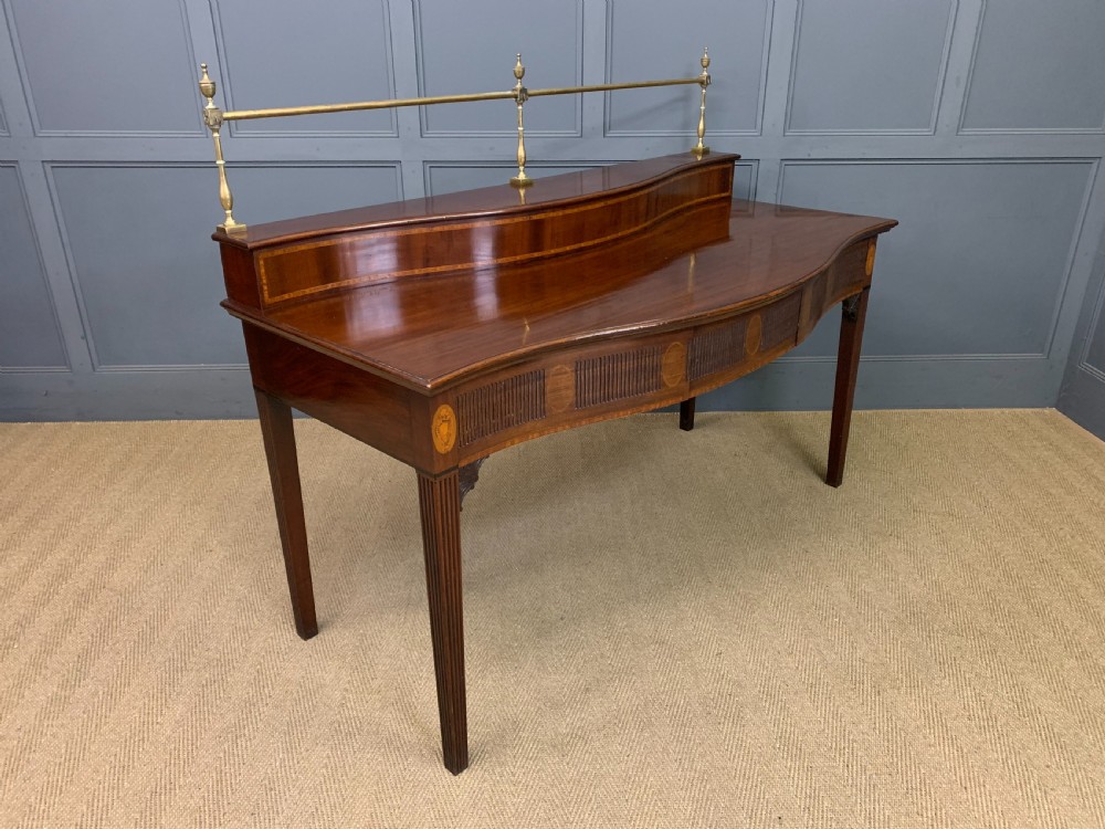 A George III mahogany serving table featuring a serpentine front, inlaid fluted detailing, square tapered legs, and a brass gallery rail. View XIII
