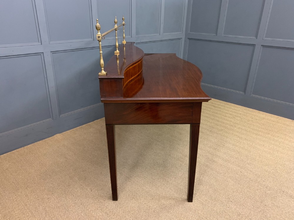 A George III mahogany serving table featuring a serpentine front, inlaid fluted detailing, square tapered legs, and a brass gallery rail. View XIV