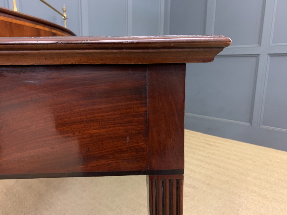 A George III mahogany serving table featuring a serpentine front, inlaid fluted detailing, square tapered legs, and a brass gallery rail. View XVI