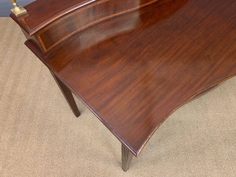 A George III mahogany serving table featuring a serpentine front, inlaid fluted detailing, square tapered legs, and a brass gallery rail. View XVII