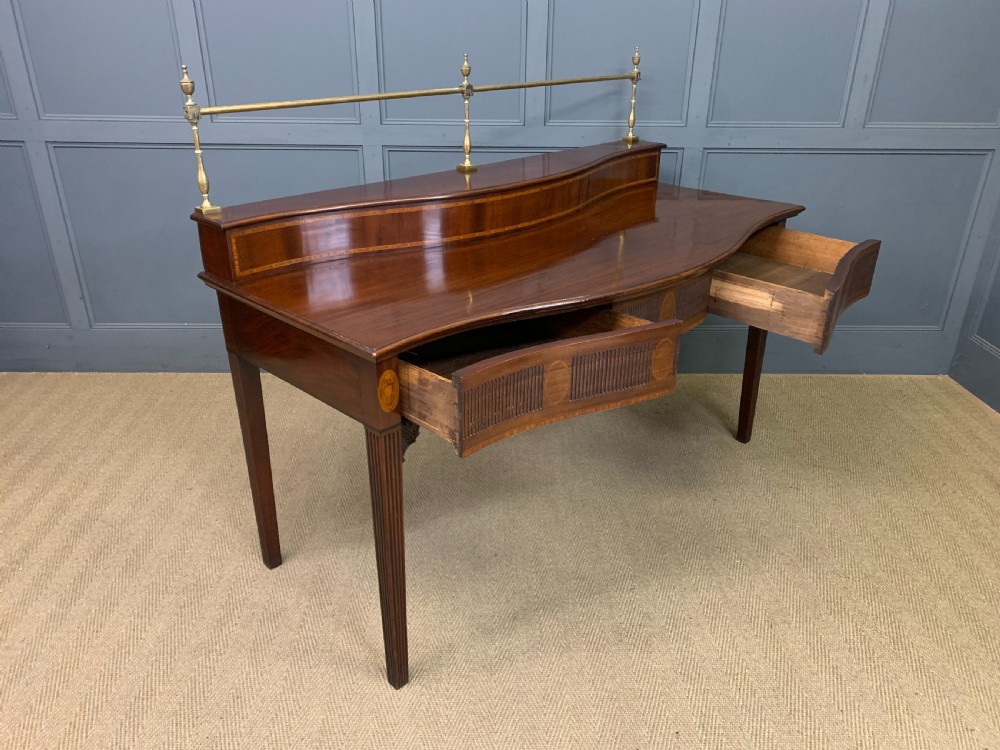 A George III mahogany serving table featuring a serpentine front, inlaid fluted detailing, square tapered legs, and a brass gallery rail. View XVIII