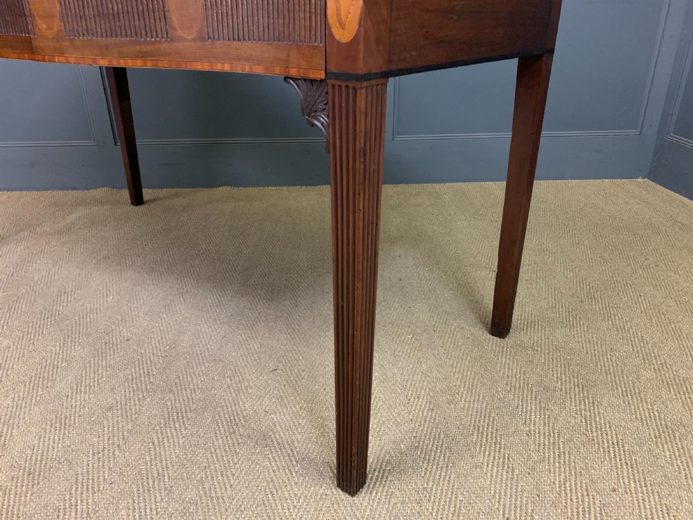 A George III mahogany serving table featuring a serpentine front, inlaid fluted detailing, square tapered legs, and a brass gallery rail. View XX