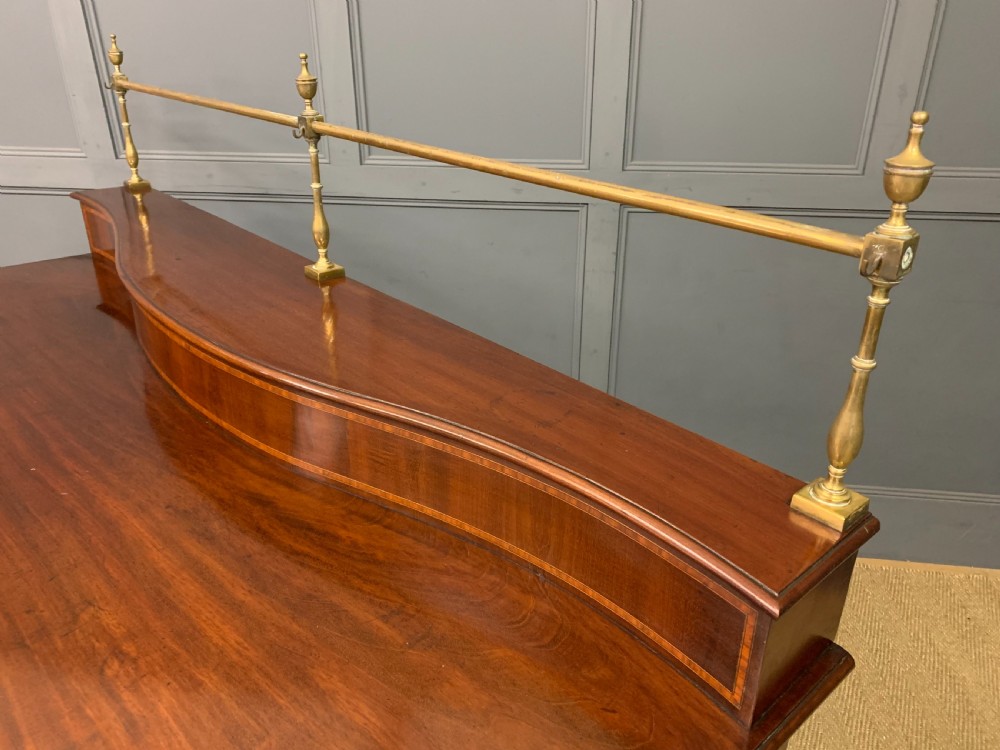 A George III mahogany serving table featuring a serpentine front, inlaid fluted detailing, square tapered legs, and a brass gallery rail. View XXI