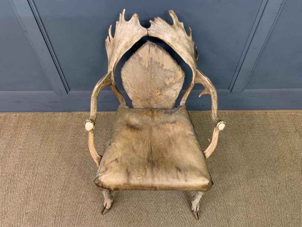 A nineteenth-century armchair constructed from natural stag antlers with a natural hide upholstered seat and backrest, featuring hoof legs. View II