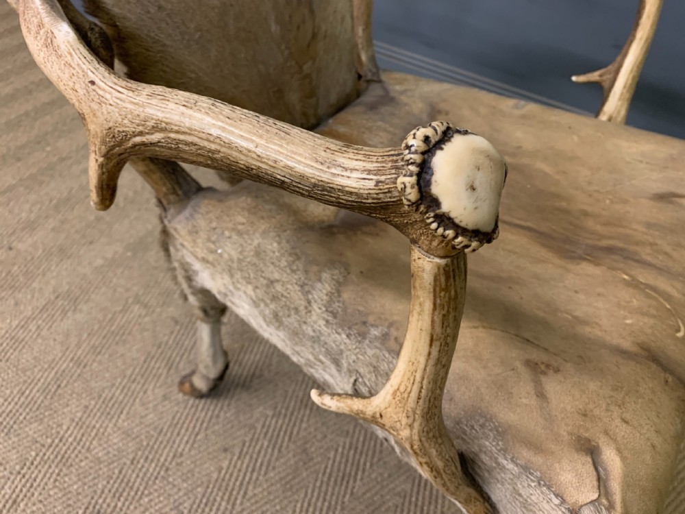 A nineteenth-century armchair constructed from natural stag antlers with a natural hide upholstered seat and backrest, featuring hoof legs. View IX