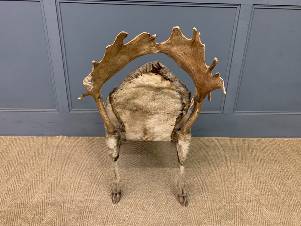 A nineteenth-century armchair constructed from natural stag antlers with a natural hide upholstered seat and backrest, featuring hoof legs. View X
