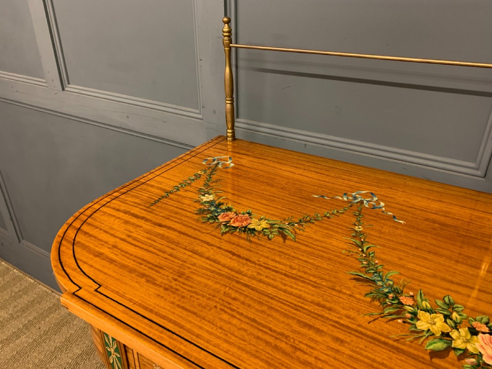A painted satinwood side table featuring hand-painted floral swags, a single drawer, a lower shelf, tapered square legs, and a raised brass gallery rail. View VII