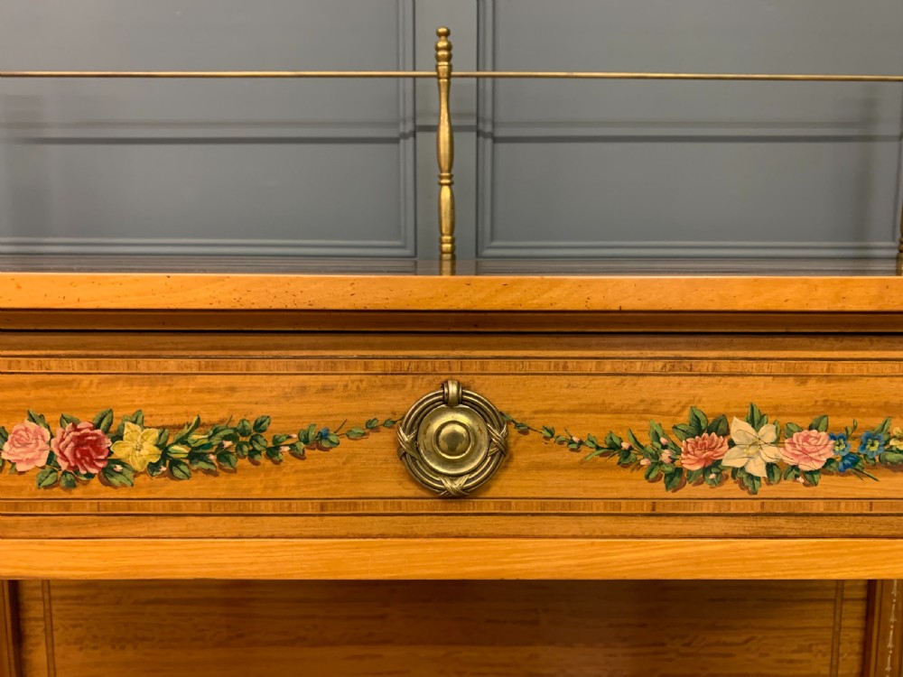 A painted satinwood side table featuring hand-painted floral swags, a single drawer, a lower shelf, tapered square legs, and a raised brass gallery rail. View IX