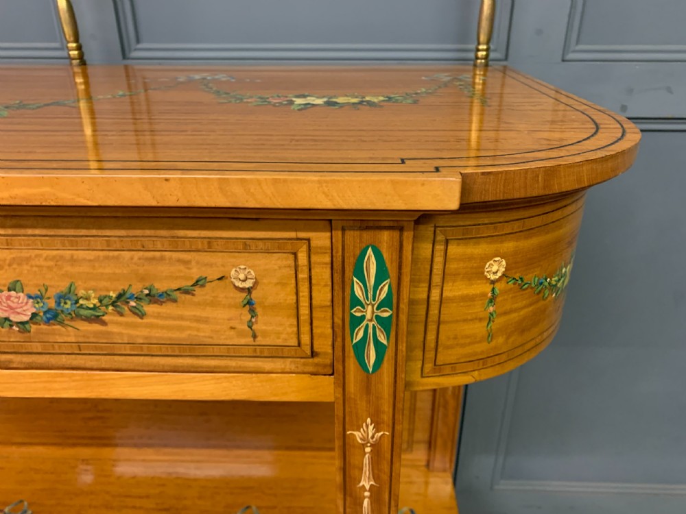A painted satinwood side table featuring hand-painted floral swags, a single drawer, a lower shelf, tapered square legs, and a raised brass gallery rail. View XIII