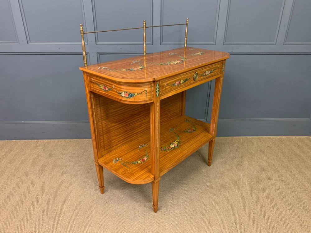 A painted satinwood side table featuring hand-painted floral swags, a single drawer, a lower shelf, tapered square legs, and a raised brass gallery rail. View XV