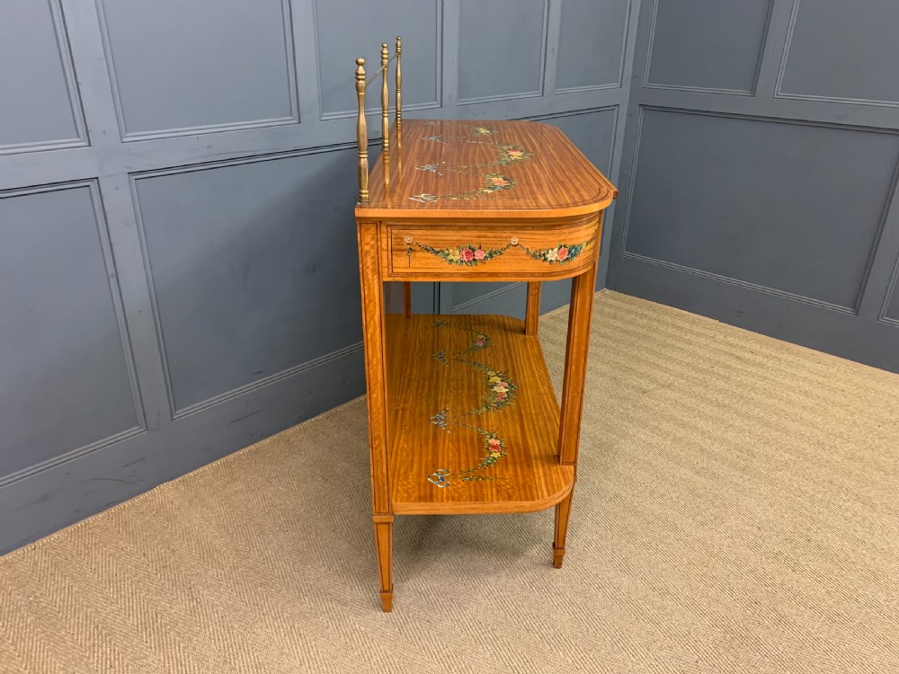 A painted satinwood side table featuring hand-painted floral swags, a single drawer, a lower shelf, tapered square legs, and a raised brass gallery rail. View XVI