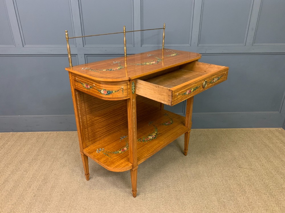 A painted satinwood side table featuring hand-painted floral swags, a single drawer, a lower shelf, tapered square legs, and a raised brass gallery rail. View XVIII