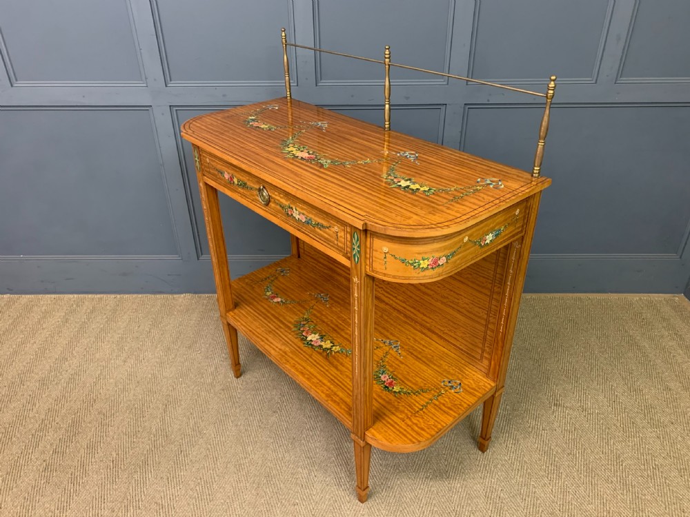 A painted satinwood side table featuring hand-painted floral swags, a single drawer, a lower shelf, tapered square legs, and a raised brass gallery rail. View XIX