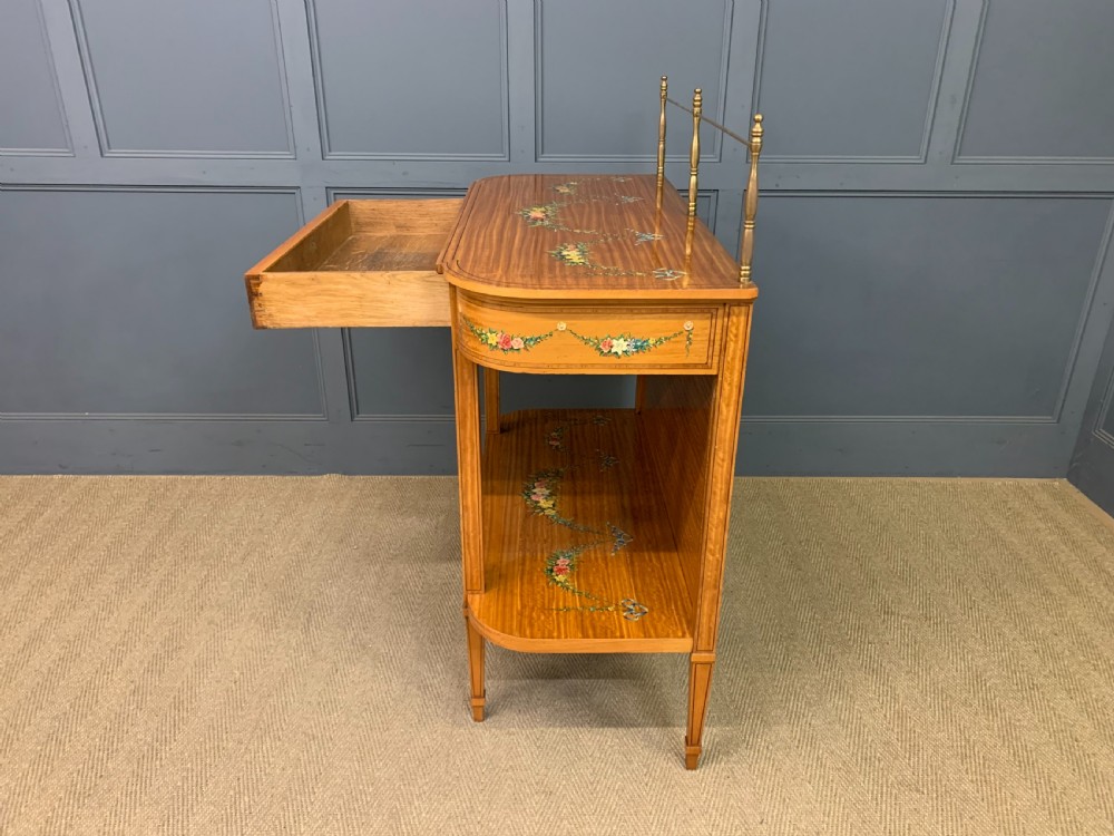 A painted satinwood side table featuring hand-painted floral swags, a single drawer, a lower shelf, tapered square legs, and a raised brass gallery rail. View XXI