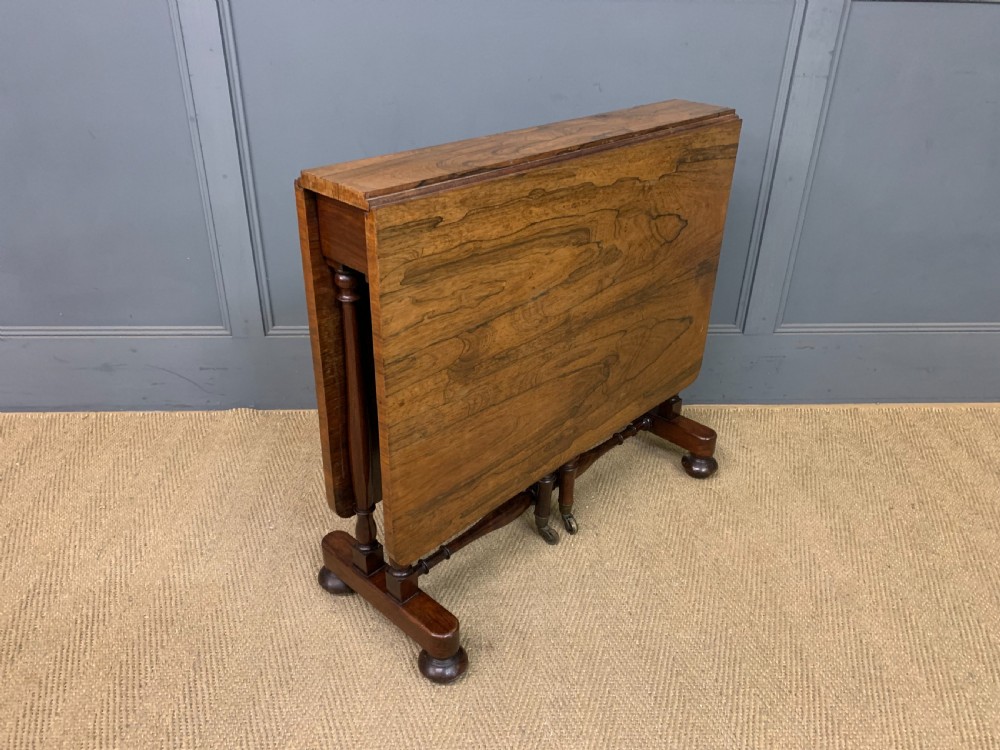 A William IV rosewood Sutherland table featuring folded drop-leaf sides, turned supports, and platform feet with castors.
