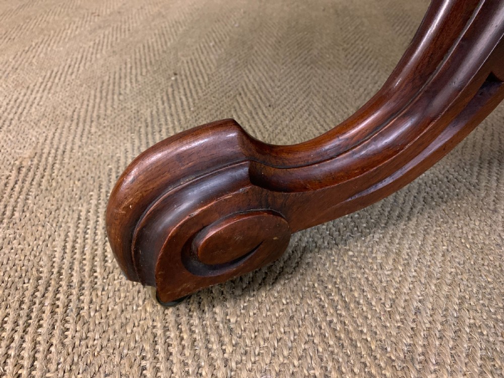 An oval Victorian rosewood loo table featuring a book-matched veneered top, crossbanded edge, and a carved central pedestal with four splayed legs on castors. View VII