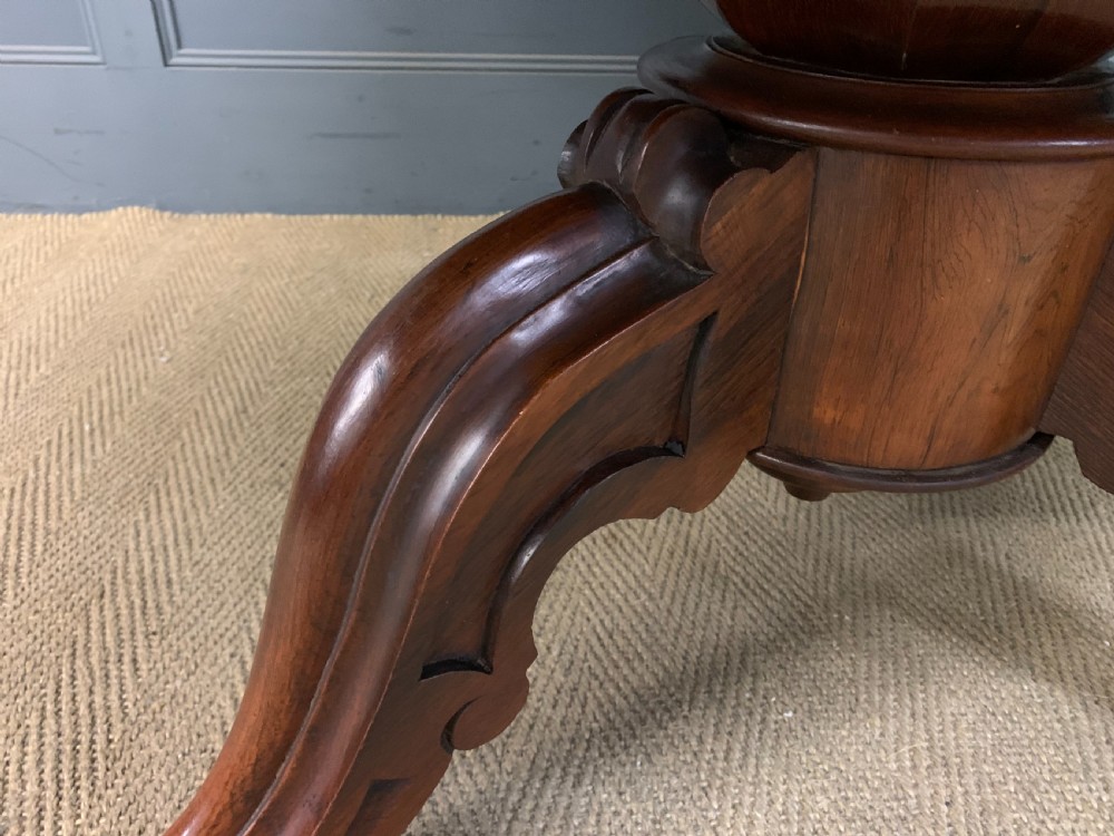 An oval Victorian rosewood loo table featuring a book-matched veneered top, crossbanded edge, and a carved central pedestal with four splayed legs on castors. View VIII