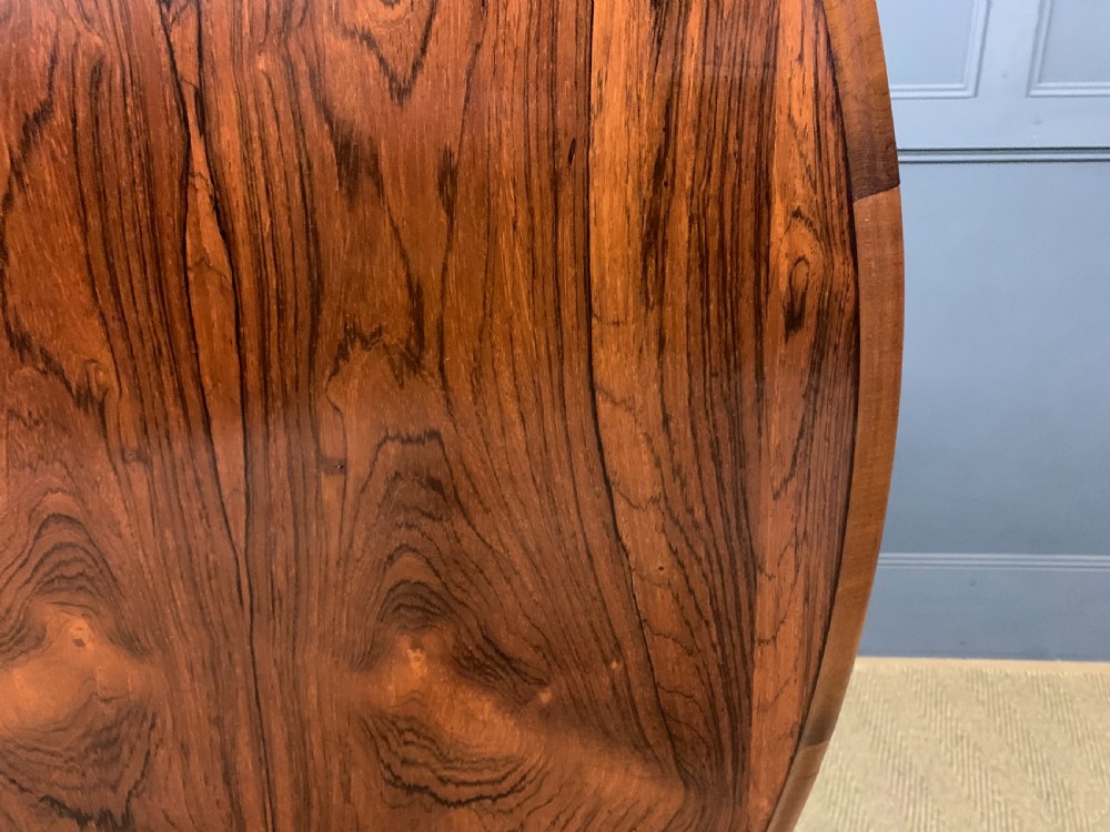 An oval Victorian rosewood loo table featuring a book-matched veneered top, crossbanded edge, and a carved central pedestal with four splayed legs on castors. View XIII