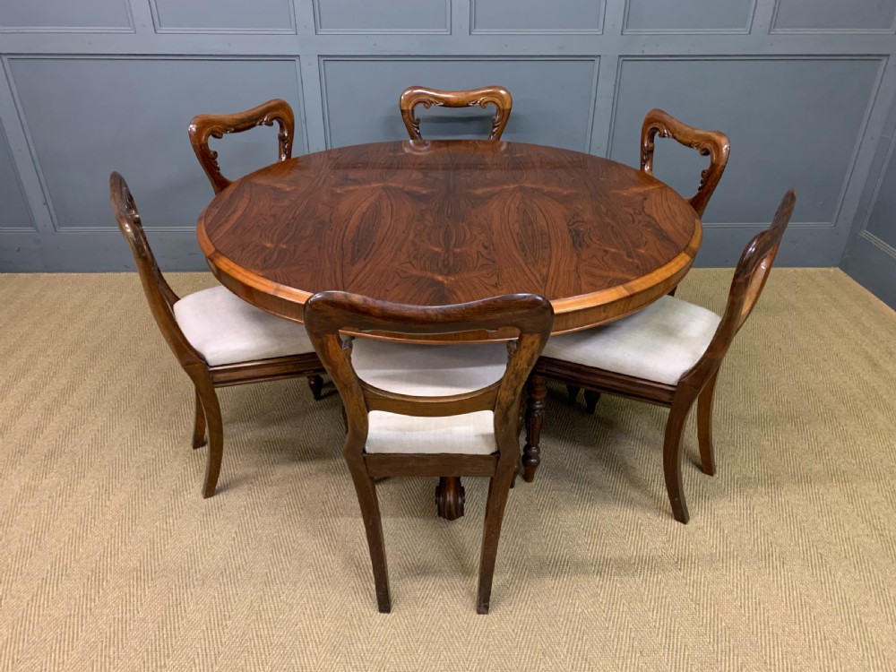 An oval Victorian rosewood loo table featuring a book-matched veneered top, crossbanded edge, and a carved central pedestal with four splayed legs on castors. View XX