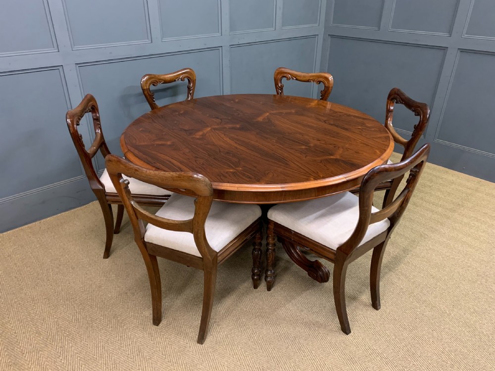 An oval Victorian rosewood loo table featuring a book-matched veneered top, crossbanded edge, and a carved central pedestal with four splayed legs on castors. View XXI