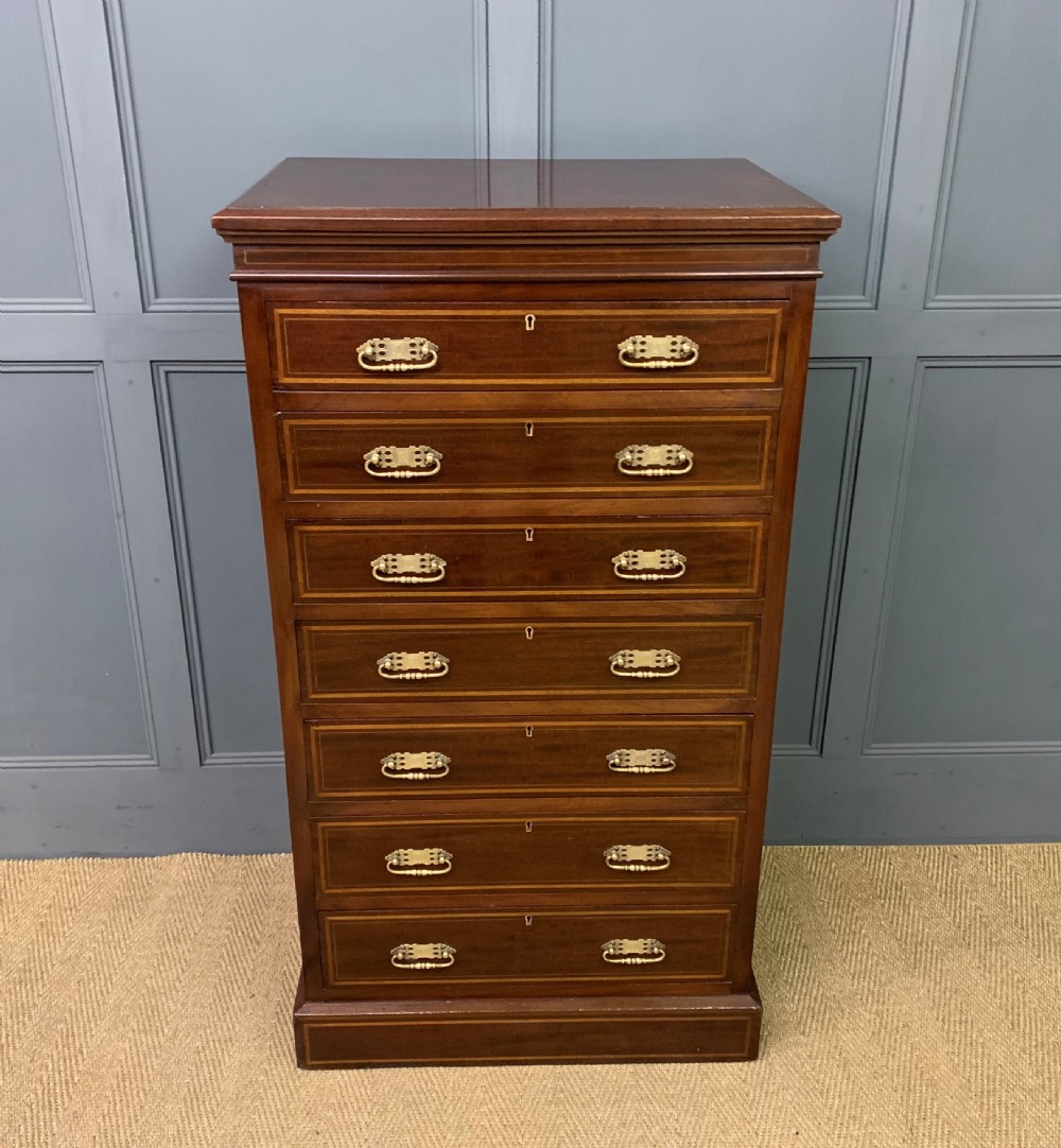 A tall Edwardian mahogany pillar chest featuring seven inlaid drawers with brass drop handles on a plinth base.