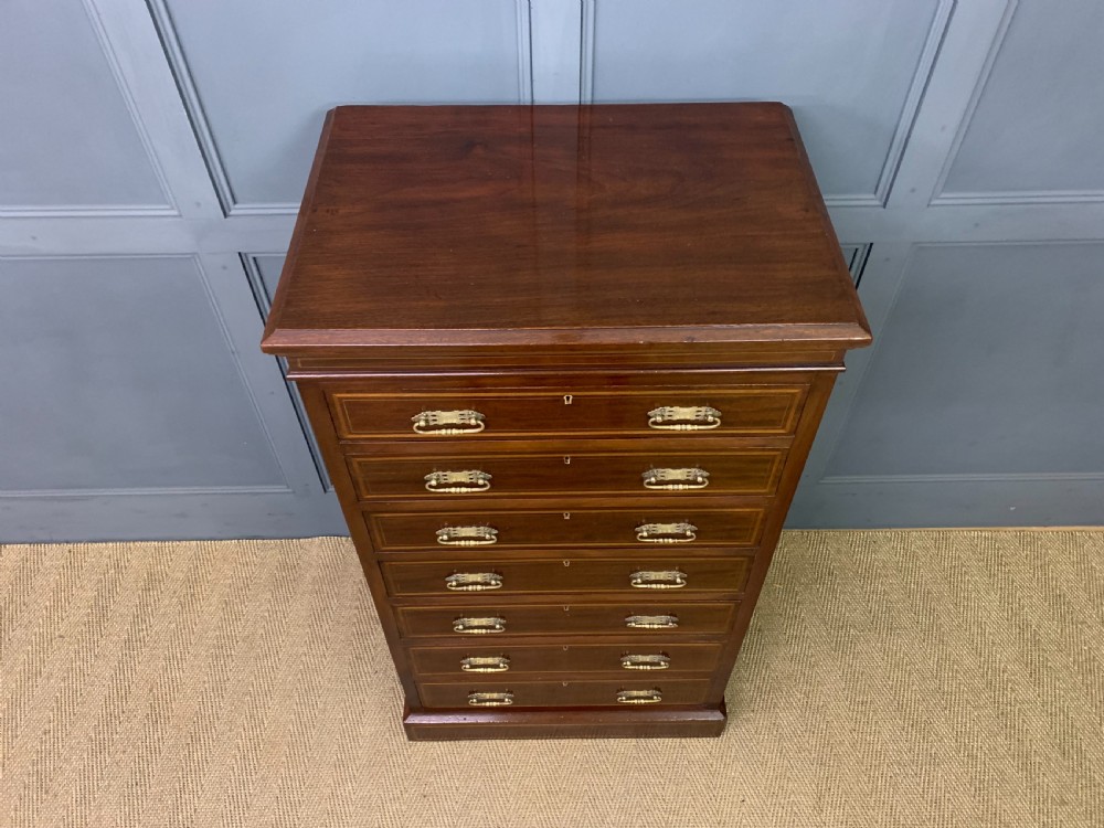A tall Edwardian mahogany pillar chest featuring seven inlaid drawers with brass drop handles on a plinth base. View IV