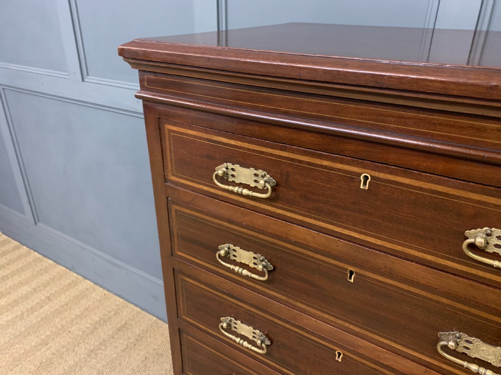 A tall Edwardian mahogany pillar chest featuring seven inlaid drawers with brass drop handles on a plinth base. View VI
