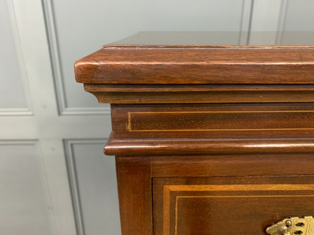 A tall Edwardian mahogany pillar chest featuring seven inlaid drawers with brass drop handles on a plinth base. View IX