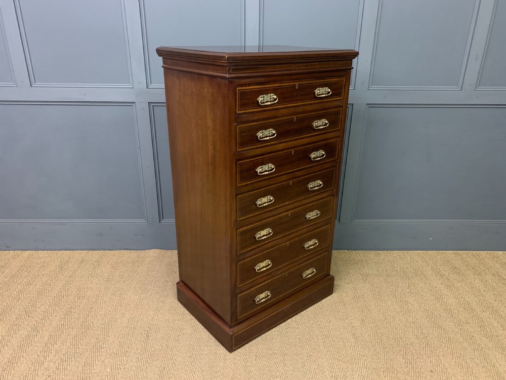 A tall Edwardian mahogany pillar chest featuring seven inlaid drawers with brass drop handles on a plinth base. View X
