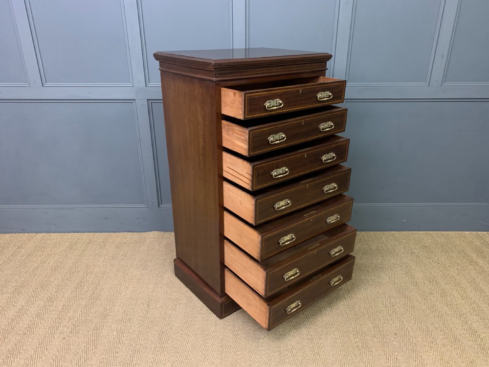 A tall Edwardian mahogany pillar chest featuring seven inlaid drawers with brass drop handles on a plinth base. View XII
