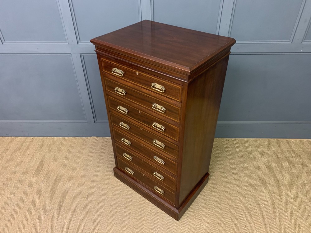 A tall Edwardian mahogany pillar chest featuring seven inlaid drawers with brass drop handles on a plinth base. View XIII