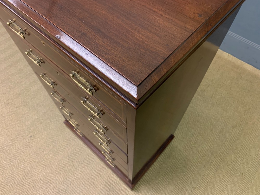 A tall Edwardian mahogany pillar chest featuring seven inlaid drawers with brass drop handles on a plinth base. View XV