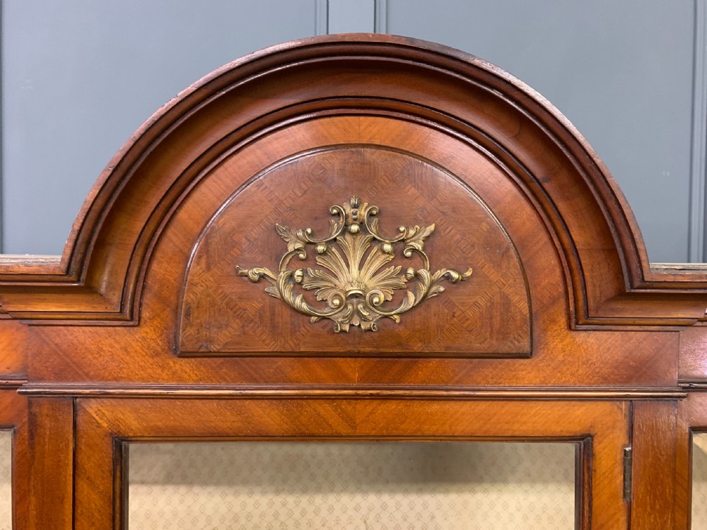 An Edwardian walnut and kingwood display cabinet featuring three glazed doors, parquetry panel lower sections, and a central arched pediment with a gilt mount. View III