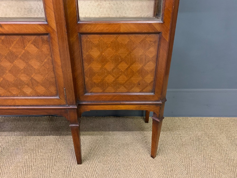 An Edwardian walnut and kingwood display cabinet featuring three glazed doors, parquetry panel lower sections, and a central arched pediment with a gilt mount. View IV