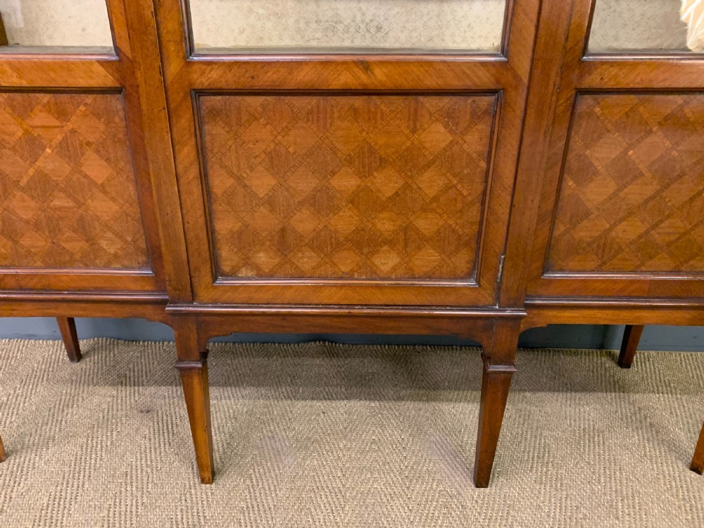 An Edwardian walnut and kingwood display cabinet featuring three glazed doors, parquetry panel lower sections, and a central arched pediment with a gilt mount. View V
