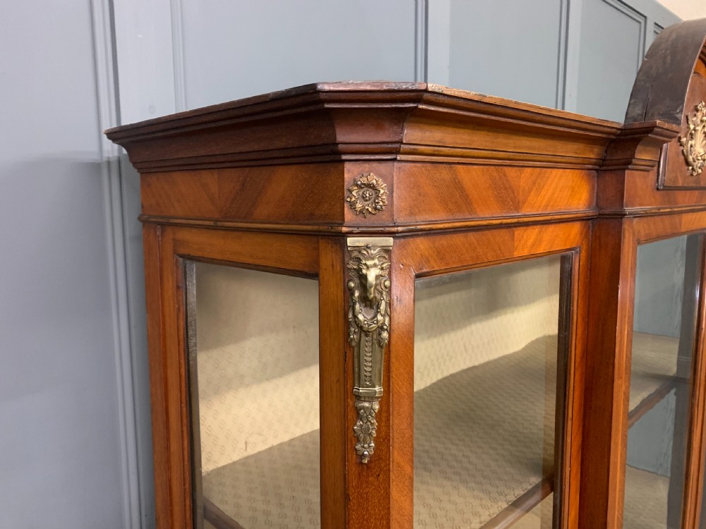 An Edwardian walnut and kingwood display cabinet featuring three glazed doors, parquetry panel lower sections, and a central arched pediment with a gilt mount. View VI