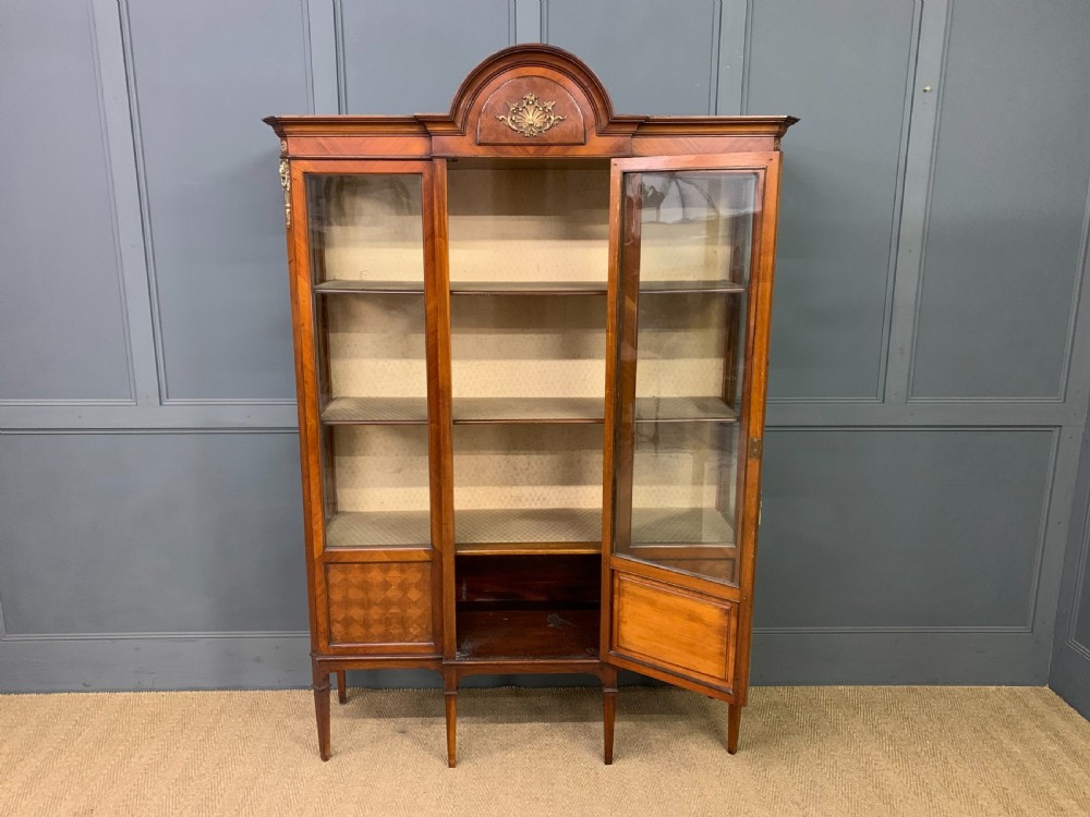 An Edwardian walnut and kingwood display cabinet featuring three glazed doors, parquetry panel lower sections, and a central arched pediment with a gilt mount. View VII