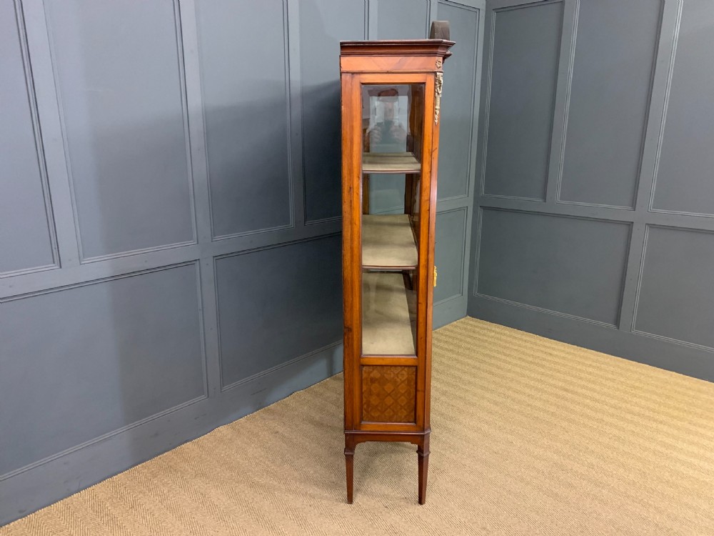 An Edwardian walnut and kingwood display cabinet featuring three glazed doors, parquetry panel lower sections, and a central arched pediment with a gilt mount. View IX