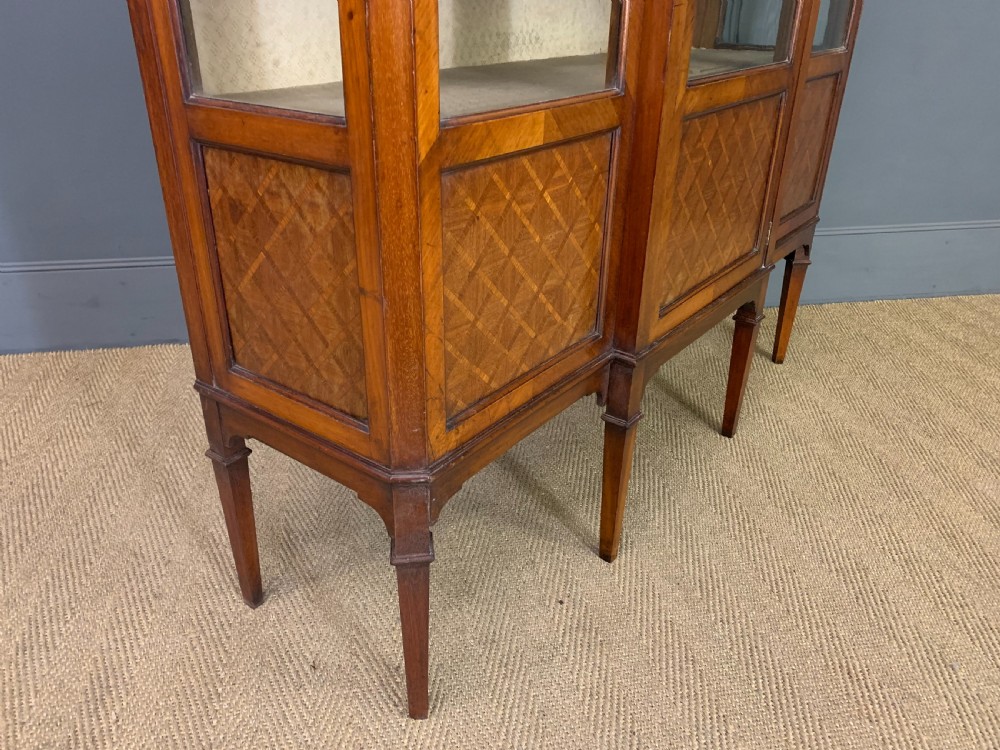 An Edwardian walnut and kingwood display cabinet featuring three glazed doors, parquetry panel lower sections, and a central arched pediment with a gilt mount. View XI