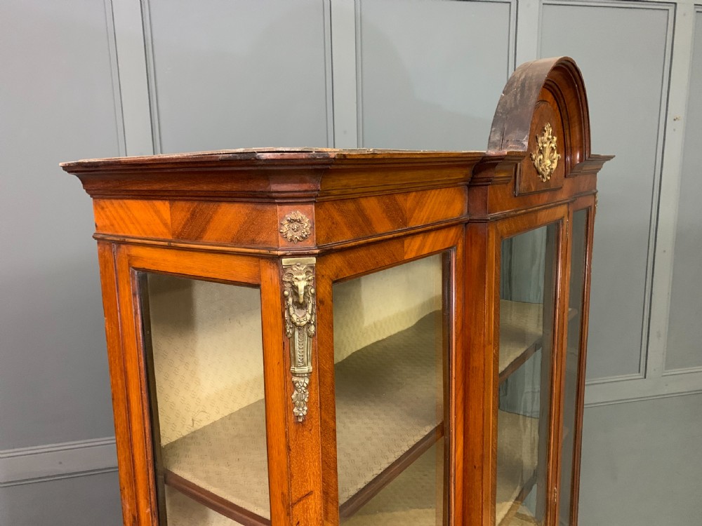 An Edwardian walnut and kingwood display cabinet featuring three glazed doors, parquetry panel lower sections, and a central arched pediment with a gilt mount. View XII