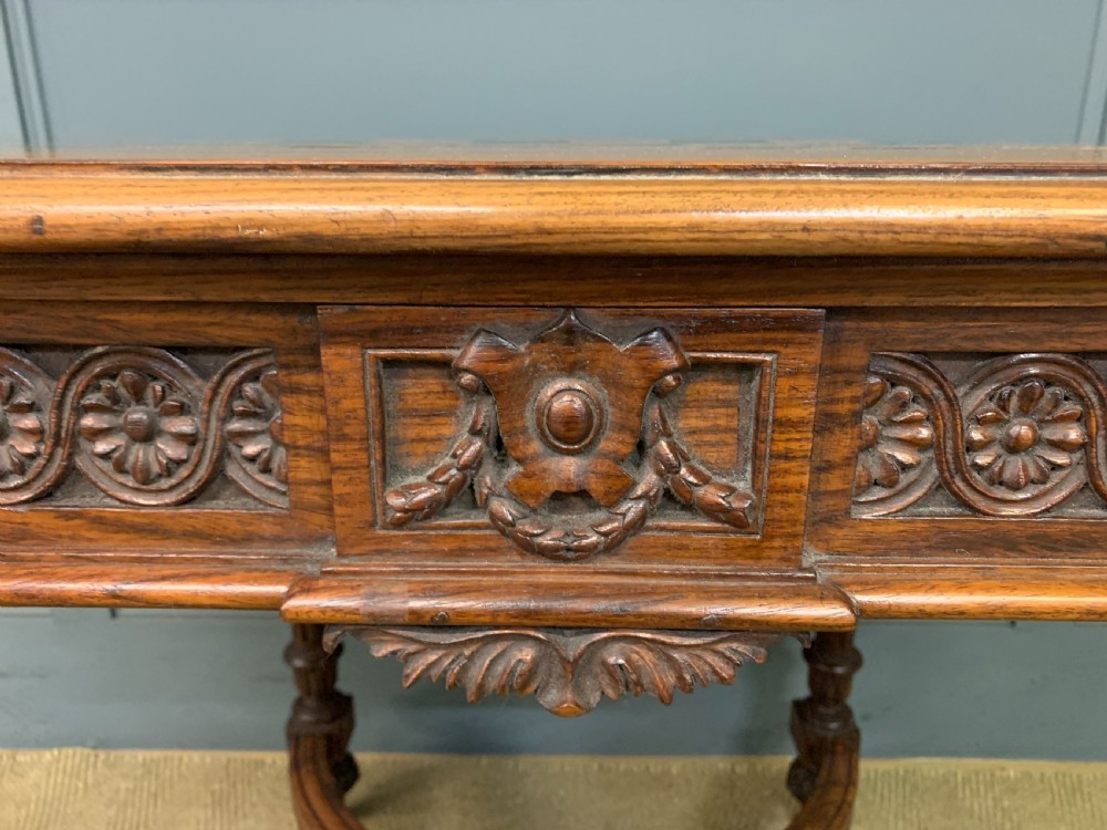 An Anglo-Indian rosewood games table featuring an inlaid square chessboard top, drop leaves, a carved frieze, and turned legs connected by a curved stretcher. View V