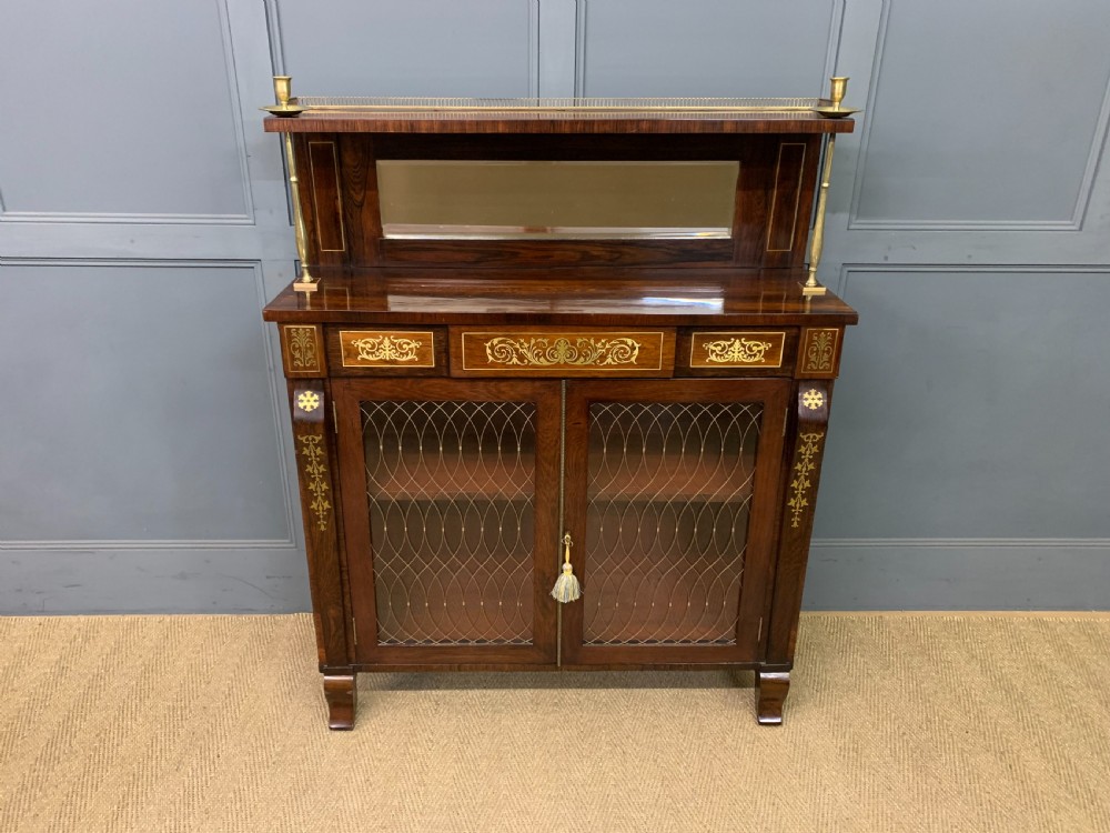 An antique Regency rosewood chiffonier featuring ornate brass inlay, a top mirror back with a brass gallery rail, and twin doors with brass wire mesh.