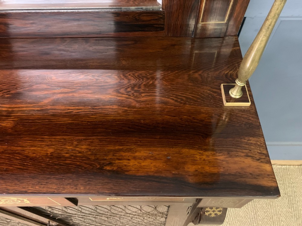 An antique Regency rosewood chiffonier featuring ornate brass inlay, a top mirror back with a brass gallery rail, and twin doors with brass wire mesh. View VI