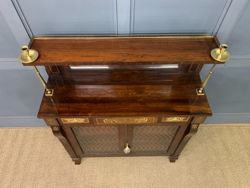 An antique Regency rosewood chiffonier featuring ornate brass inlay, a top mirror back with a brass gallery rail, and twin doors with brass wire mesh. View VII