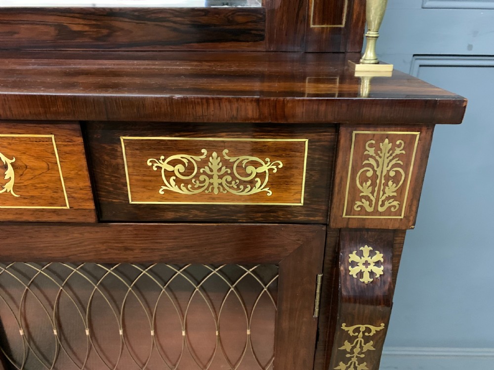An antique Regency rosewood chiffonier featuring ornate brass inlay, a top mirror back with a brass gallery rail, and twin doors with brass wire mesh. View VIII