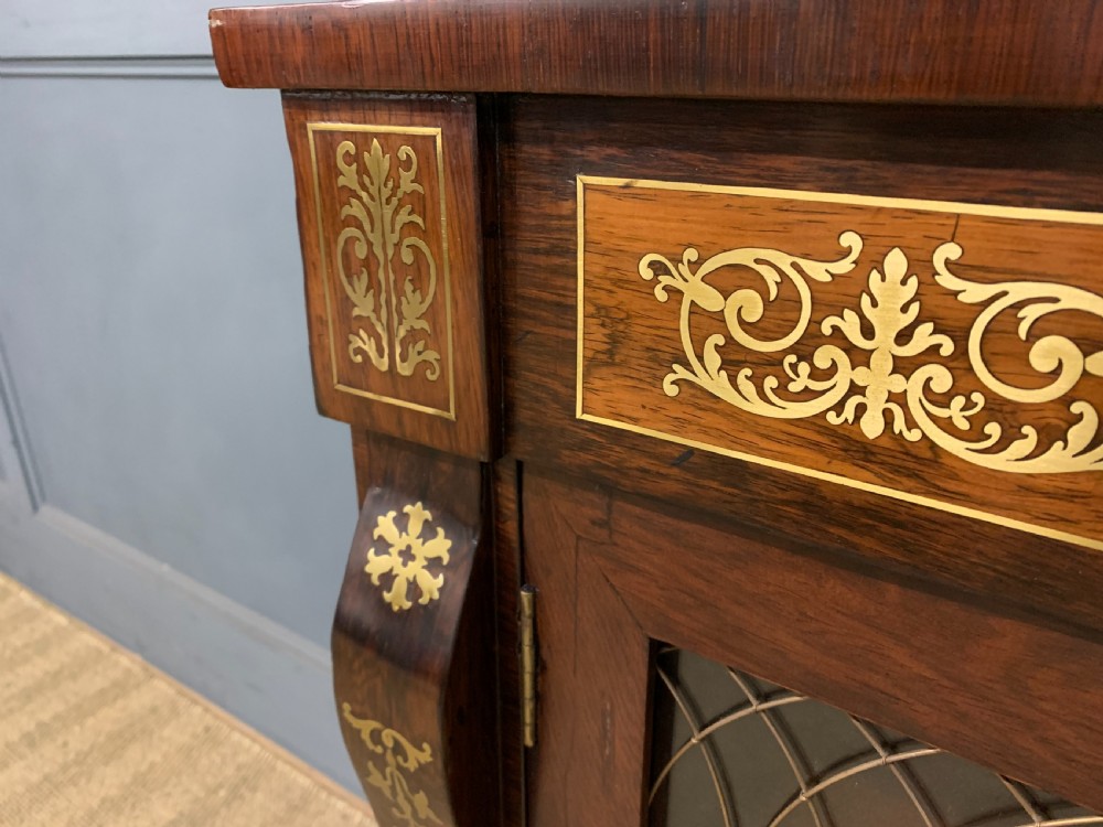 An antique Regency rosewood chiffonier featuring ornate brass inlay, a top mirror back with a brass gallery rail, and twin doors with brass wire mesh. View IX