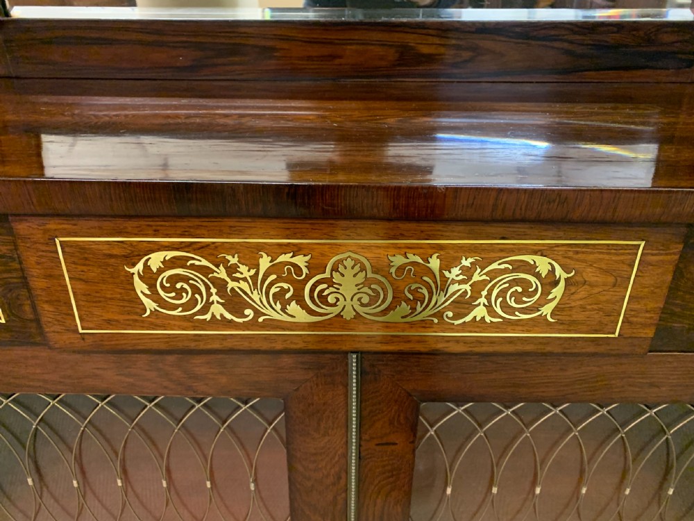 An antique Regency rosewood chiffonier featuring ornate brass inlay, a top mirror back with a brass gallery rail, and twin doors with brass wire mesh. View X