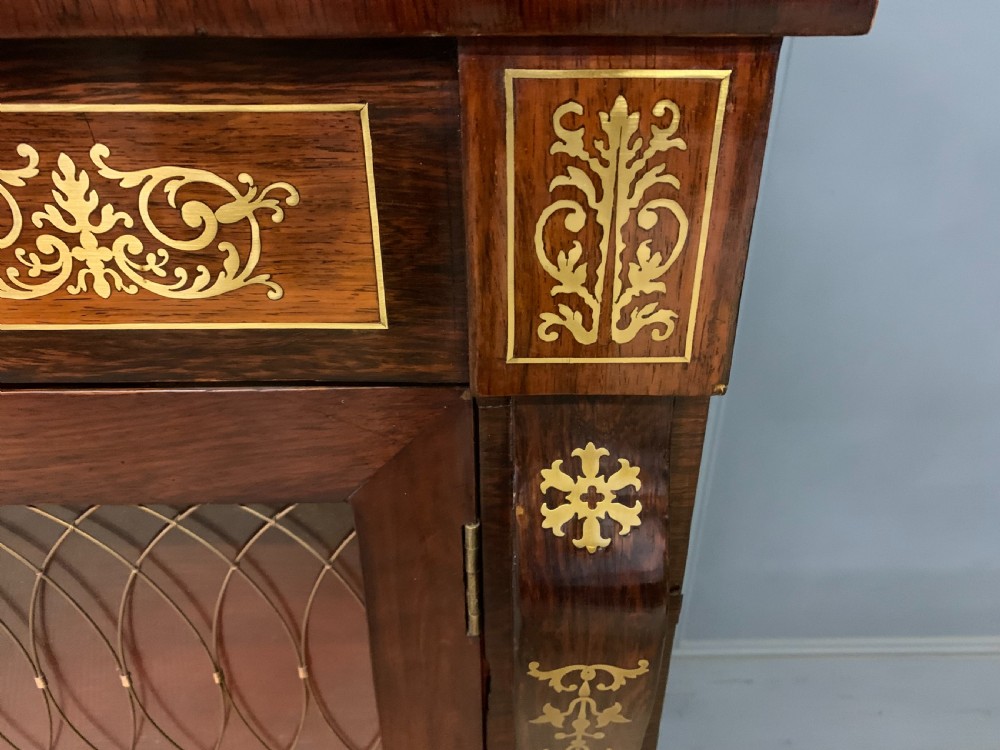 An antique Regency rosewood chiffonier featuring ornate brass inlay, a top mirror back with a brass gallery rail, and twin doors with brass wire mesh. View XI